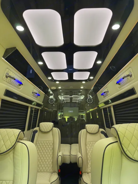 Inside a plush **rv rental**: light cream quilted seats, dark wood-paneled walls, bright ceiling panels, and blue accent lighting.. Mercedes-Benz Sprinter 2025