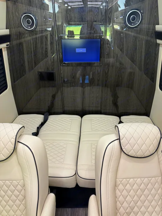 Plush, cream leather interior of a luxury RV rental, featuring diamond-stitched seats, wood paneling, and an entertainment screen.. Mercedes-Benz Sprinter 2025