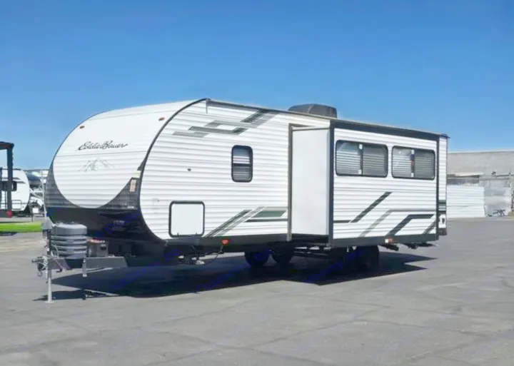 A white Eddie Bauer travel trailer RV rental with black and green accents, parked under a blue sky, ready for adventure.. Heartland RVs Eddie Bauer EBS 261BH 2024
