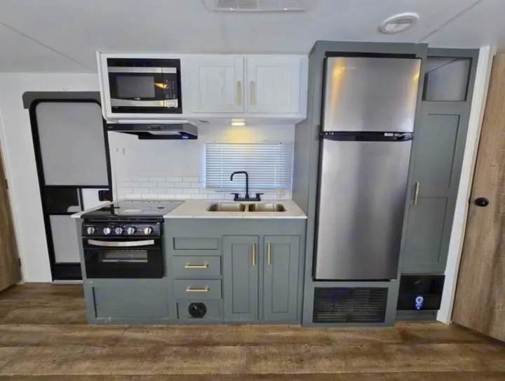 Modern RV rental kitchen with full fridge, microwave, and stove. Sleek grey cabinets & wood flooring for comfortable travel.. Heartland RVs Eddie Bauer EBS 261BH 2024