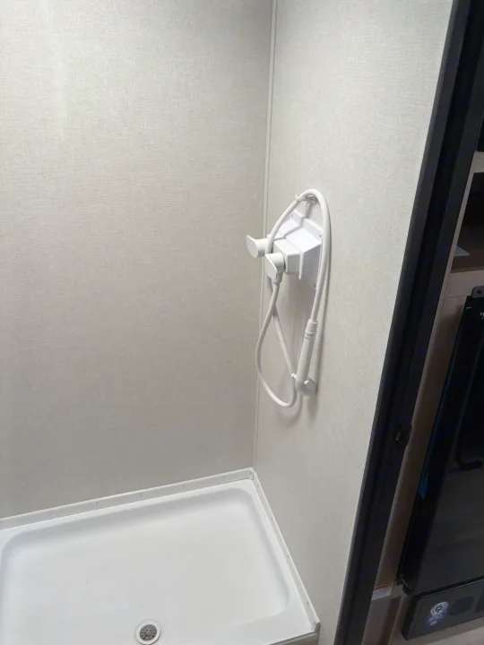 Simple RV rental shower stall with light gray textured walls, white shower pan, and a mounted handheld showerhead.. Keystone RV Coleman 2025