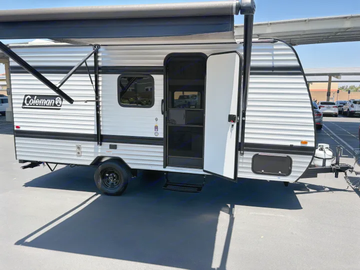 White Coleman travel trailer for rv rental with an extended black awning, open door, and visible steps.. Keystone RV Coleman 2025