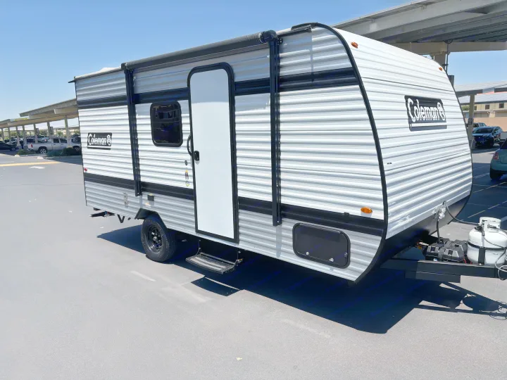 Sunny view of a Coleman travel trailer (RV rental) with a gray and white exterior, side door, and awning.. Keystone RV Coleman 2025