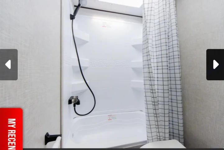 Explore our RV rental: A clean, compact shower with a white tub, handheld spray, and a modern plaid curtain.. Jayco Jay Flight SLX 2025