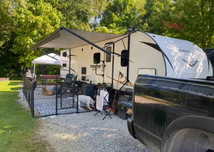 RV rental setup at a campsite with dogs in a fenced pet area under the extended awning.. Forest River Tracer Breeze 2019