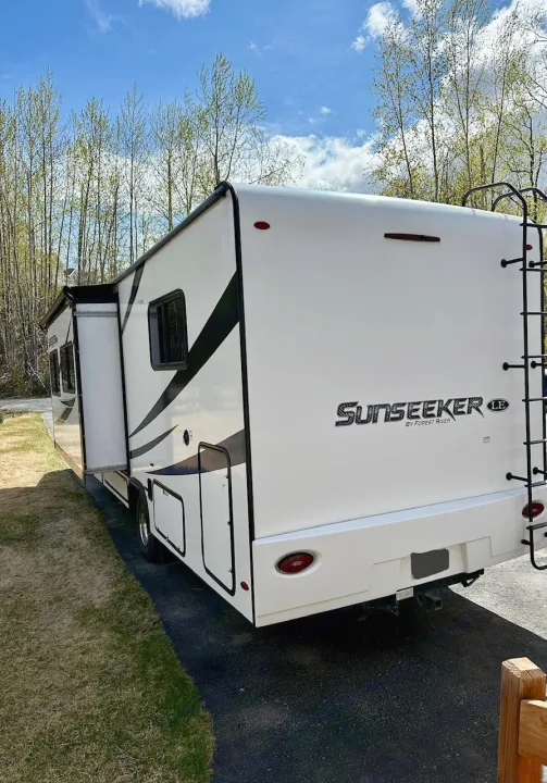 White Sunseeker motorhome, an ideal RV rental, showcasing its slide-out and rear ladder, parked on asphalt under a blue sky.. Forest River Sunseeker LE 2021