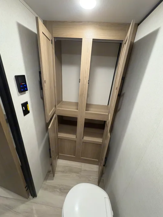 Functional RV rental bathroom featuring a toilet, built-in wooden cabinets, and wall-mounted controls for convenience.. Keystone RV Coleman 2025