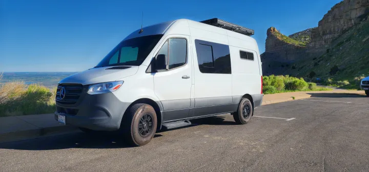 An RV rental, a white Mercedes Sprinter van, parked at a scenic viewpoint overlooking a valley and rock formations.. Mercedes Sprinter 2023