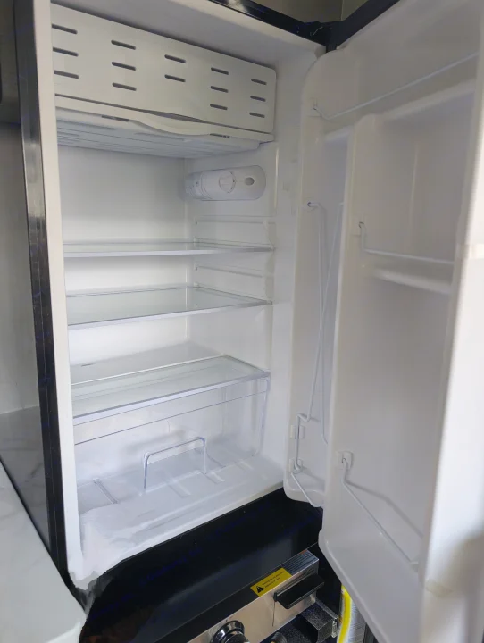 Empty, compact RV rental refrigerator. Features a top freezer, clear shelves, and crisper drawer, ready for your travel essentials.. Coachmen Viking 1200ROK 2025