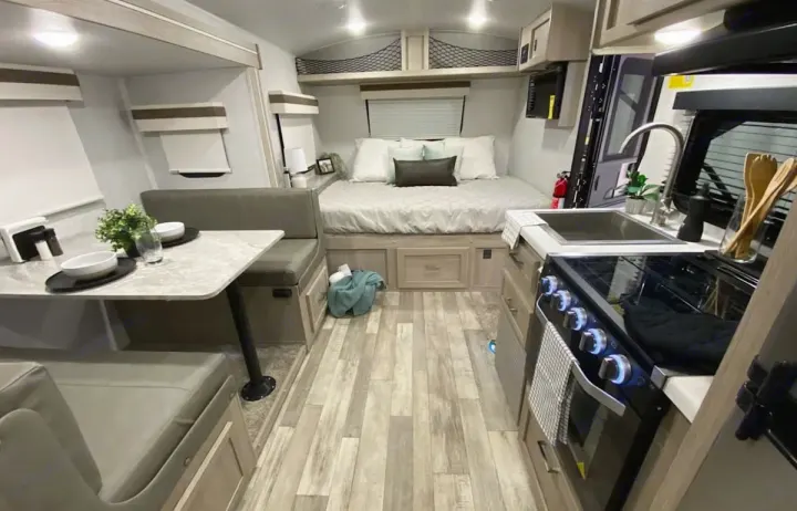 Inside an RV rental: a cozy living space with a dining booth, full-size bed, and compact kitchen, ready for travel.. Forest River Rockwood Geo Pro 2021