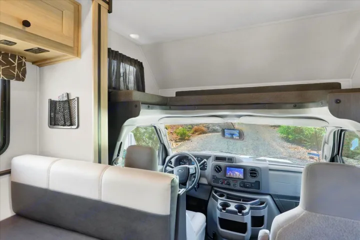 RV rental interior showing the cockpit, dashboard, and an over-cab bunk bed, with a view of a dirt road.. Forest River Sunseeker 2550 DSLE 2025