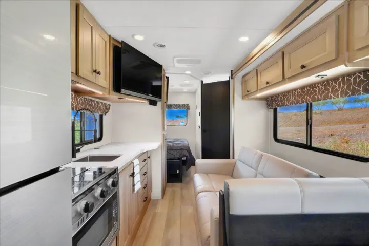 Modern rv rental interior features a full kitchen, L-shaped sofa, and a cozy bed, with scenic views from the large windows.. Forest River Sunseeker 2550 DSLE 2025