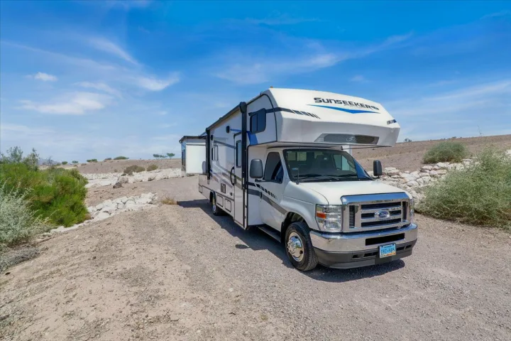 White Sunseeker RV rental parked on a gravel lot in a sunny desert landscape with scrub brush under a clear blue sky.. Forest River Sunseeker 2550 DSLE 2025
