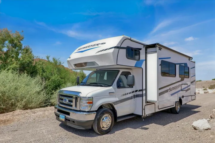 White Sunseeker RV rental parked on a dirt path with green foliage, perfect for a sunny adventure under a blue sky.. Forest River Sunseeker 2550 DSLE 2025