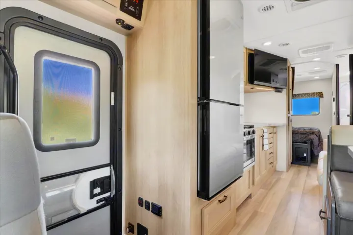 Inside a modern rv rental: entry door with a scenic view, kitchen with fridge & oven, mounted TV, and a rear bedroom.. Forest River Sunseeker 2550 DSLE 2025