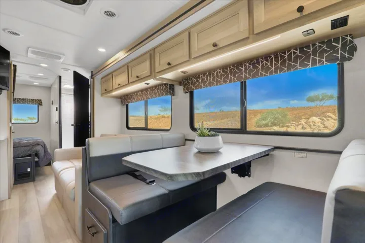 Spacious rv rental interior featuring a modern dinette, overhead storage, large windows, and bedroom access.. Forest River Sunseeker 2550 DSLE 2025