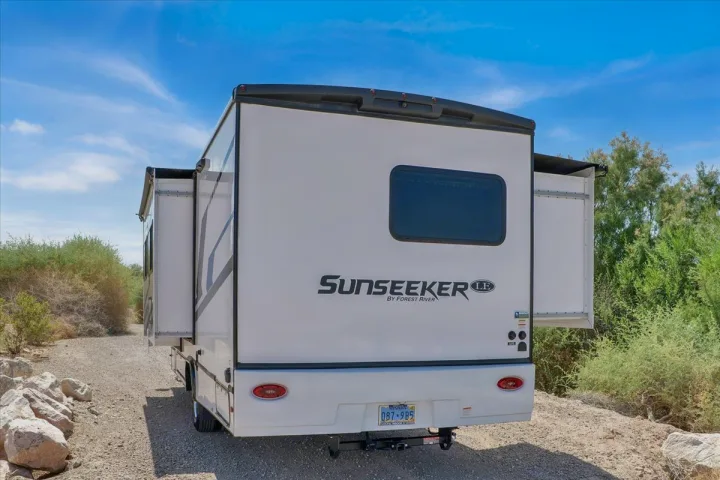 White Sunseeker RV rental parked on a dirt road, rear view showing extended slide-outs. Ideal for camping & road trips.. Forest River Sunseeker 2550 DSLE 2025