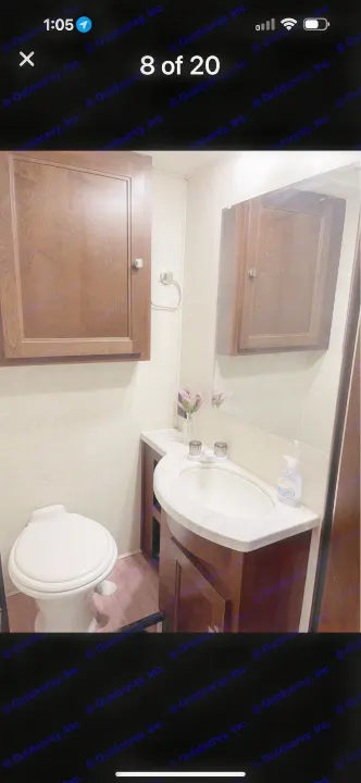 This RV rental bathroom features a white toilet, sink vanity with a marble-look counter, mirror, and dark wood cabinets.. Forest River Sunseeker LE 2019