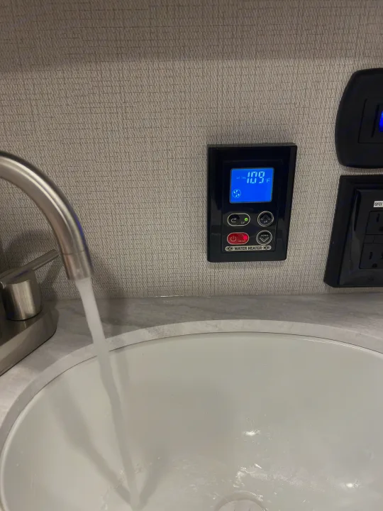 RV rental interior: Water running from faucet, with a digital water heater control showing 109°F for comfortable hot water.. Keystone RV Cougar 2023