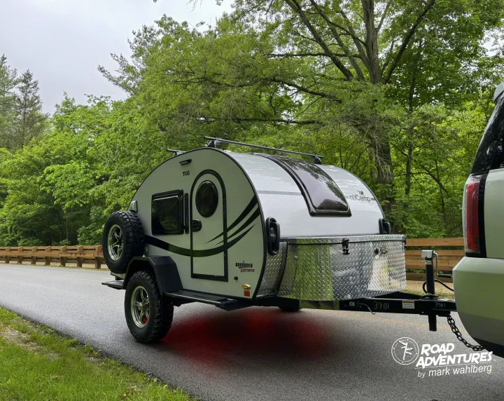 A T@G Boondock Black Canyon teardrop camper, great for an rv rental adventure, on a wet road amidst green trees.. nuCamp T@G XL 2025