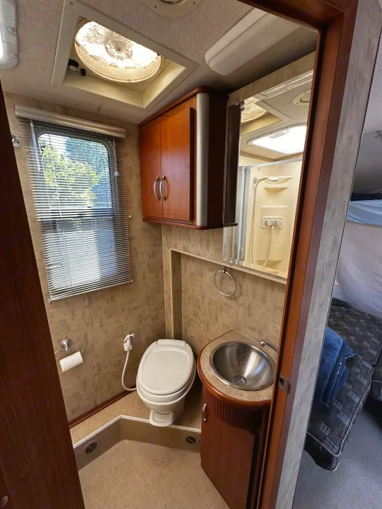 Explore a functional RV bathroom, perfect for your rv rental adventure. Includes toilet, sink, shower, window, and overhead cabinet.. Winnebago View 2006