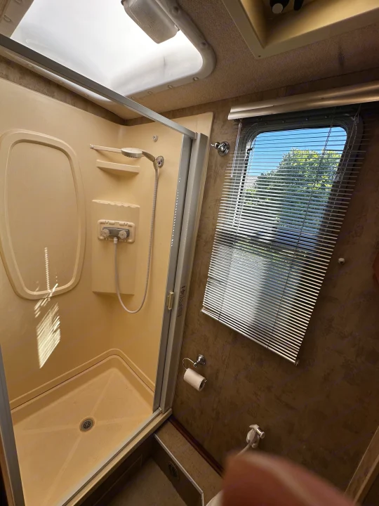 Visually impaired users: A compact RV rental bathroom features a shower, window with blinds, toilet paper holder, and overhead skylight.. Winnebago View 2006
