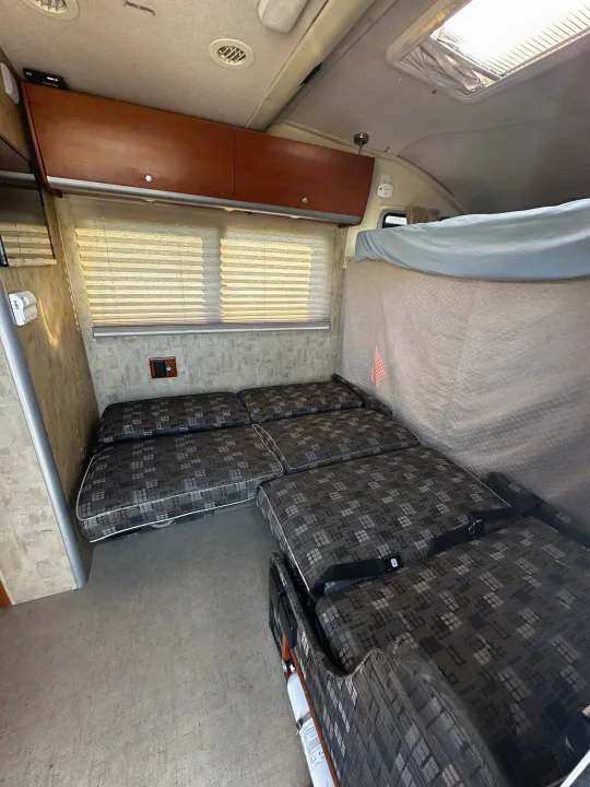 RV rental interior features a convertible dinette/bed, overhead cabinets, and window blinds, ready for your next adventure.. Winnebago View 2006