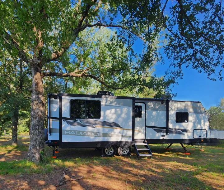 A modern Radiance travel trailer RV rental, set up in a shaded, treed campground for a perfect outdoor getaway.. Cruiser RV Radiance 2022