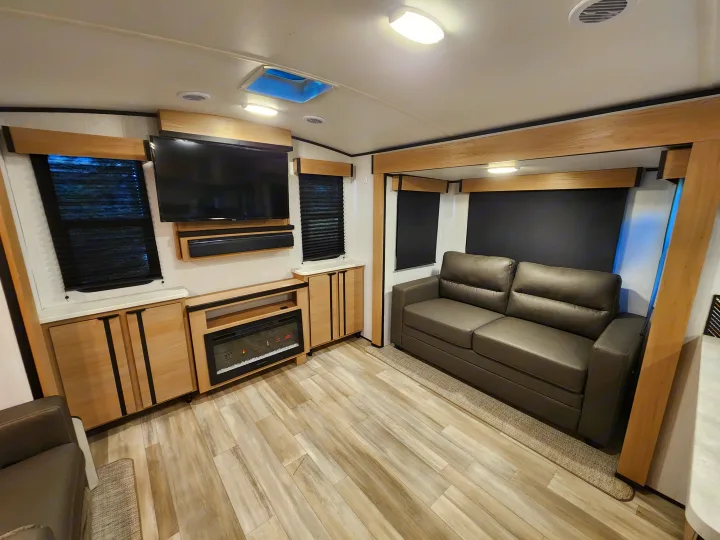 Modern RV rental living space with a comfortable sofa, entertainment setup, fireplace, and light wood flooring.. Cruiser RV Radiance 2022