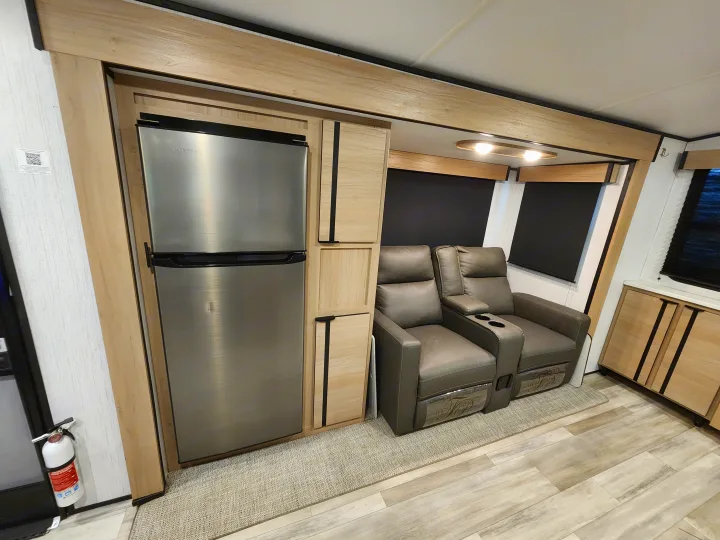 Inside a modern RV rental: stainless steel fridge, two recliners, wood cabinets, and light flooring. Compact and functional.. Cruiser RV Radiance 2022