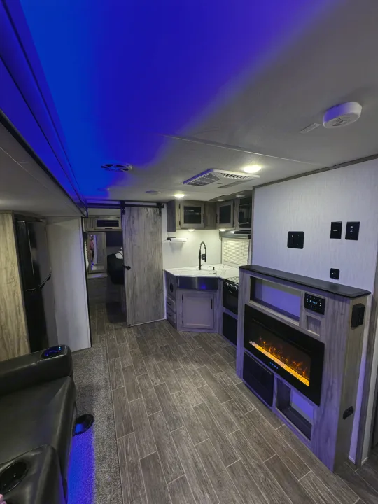 RV rental interior: modern kitchen, electric fireplace with orange glow, and cool blue ambient lighting creating a stylish space.. Forest River Cherokee Alpha Wolf 2022