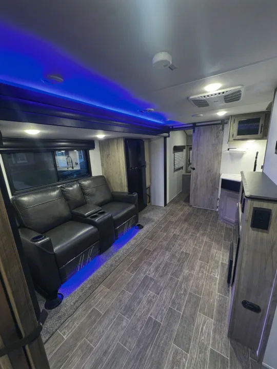 Modern RV rental interior with comfy recliners, blue accent lighting, wood-look flooring, and a kitchen area.. Forest River Cherokee Alpha Wolf 2022