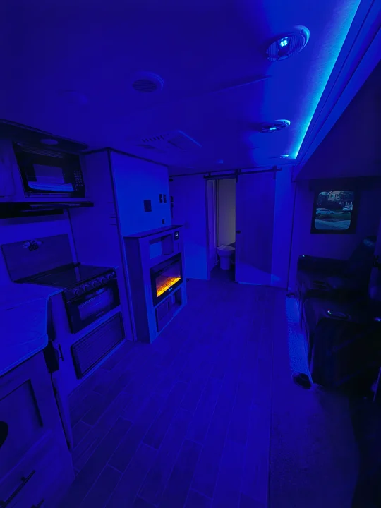 Explore this cozy RV rental interior at night, featuring a kitchen, living area, and bathroom illuminated by blue LED lights.. Forest River Cherokee Alpha Wolf 2022