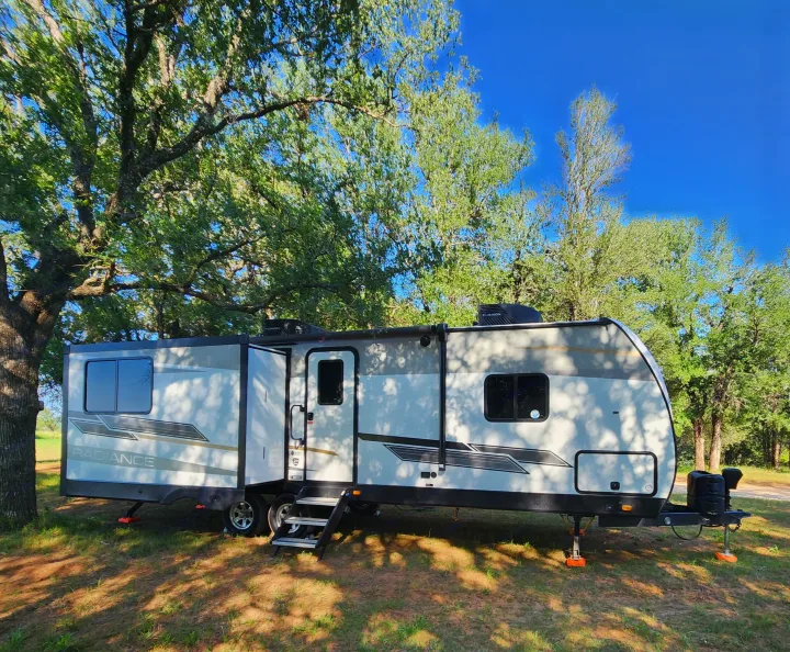 This Radiance travel trailer RV rental is set up at a leafy campsite, featuring an extended slide-out and leveling jacks.. Cruiser RV Radiance 2022