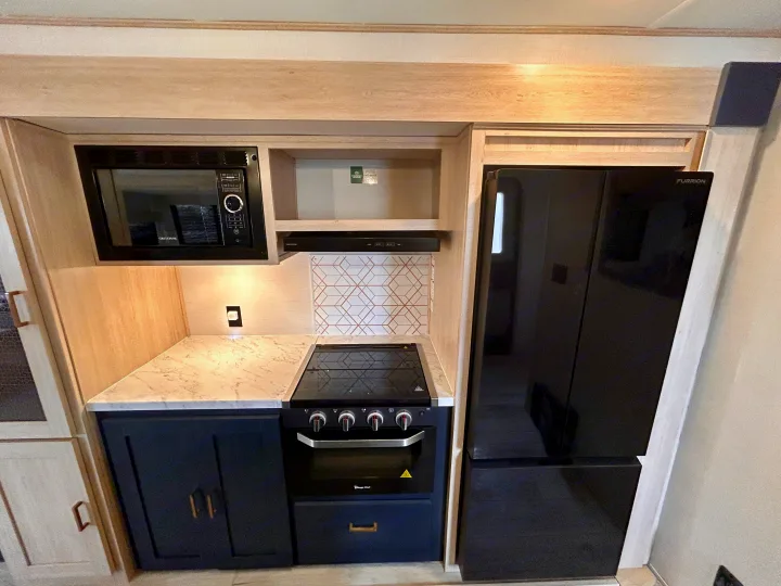 Modern RV rental kitchen features black appliances (microwave, stove, fridge), white counters, and dark blue cabinets.. Primetime Avenger 2025