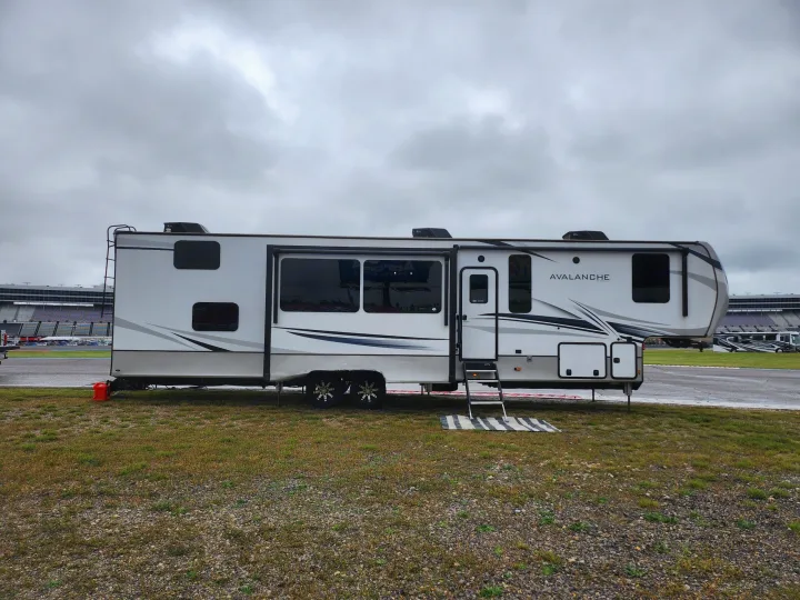 Spacious Avalanche fifth wheel RV rental parked on grass next to a race track under an overcast sky.. Keystone RV Avalanche 2023