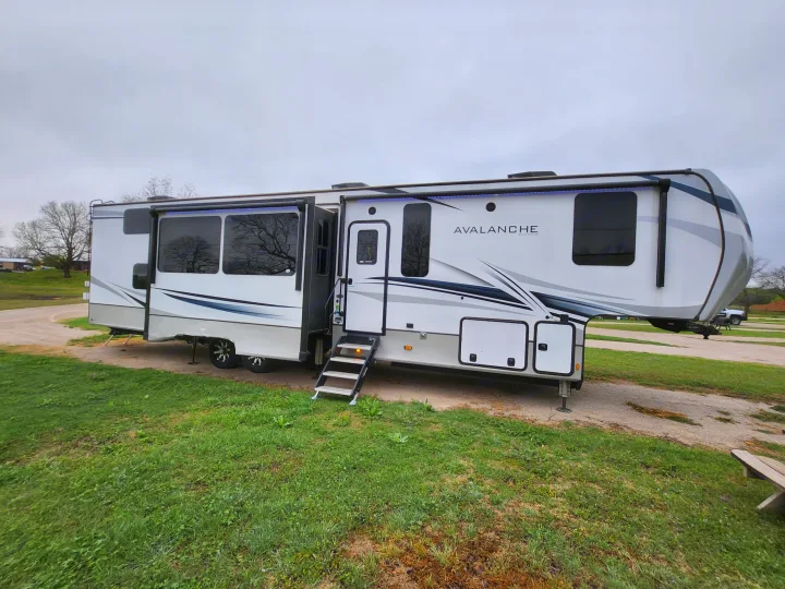 This Keystone Avalanche fifth-wheel RV is set up at a campground, perfect for an RV rental adventure.. Keystone RV Avalanche 2023
