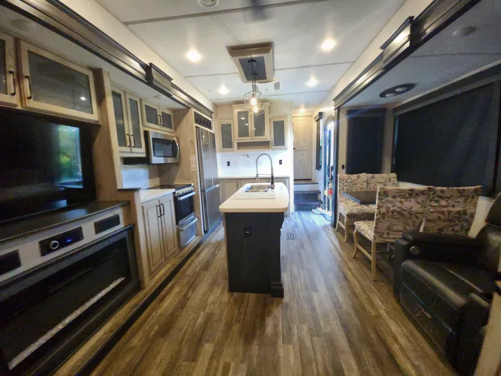 Modern RV interior features a full kitchen with island, living area with TV and fireplace. Ideal for an RV rental adventure.. Keystone RV Avalanche 2023