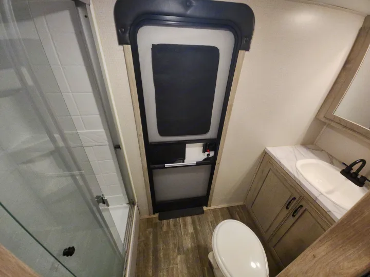 Compact RV rental bathroom with a shower, toilet, and modern vanity area featuring a sink and mirror.. Keystone RV Avalanche 2023