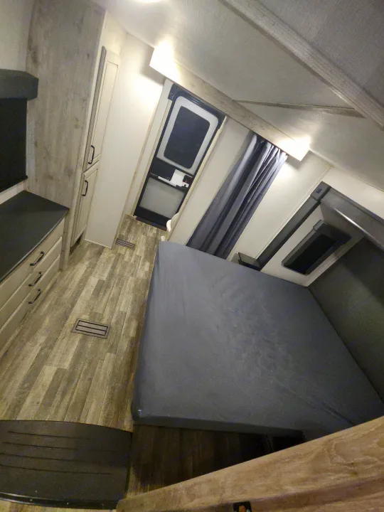 Interior of an RV rental bedroom, featuring a large gray bed, wood-look flooring, built-in dresser, and an exterior door.. Keystone RV Avalanche 2023