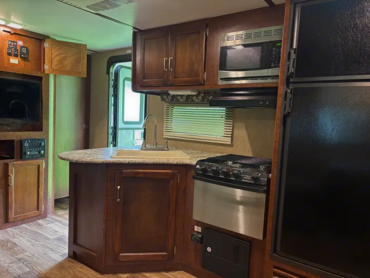 Fully equipped kitchen in an RV rental, featuring a sink, stove, microwave, fridge, and overhead cabinets.. Keystone RV Outback Ultra-Lite 2017