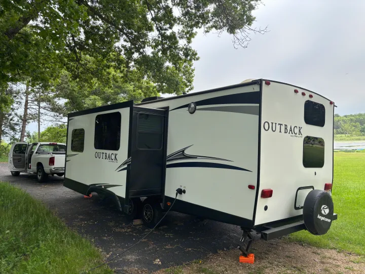RV rental parked at a lakeside campground with a pickup truck, showing its slide-out extended and power connected.. Keystone RV Outback Ultra-Lite 2017
