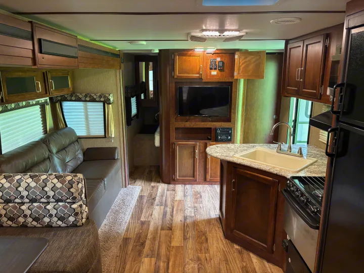 Inside this rv rental, a cozy living area with a leather couch, entertainment center, and a compact kitchen with sink and stove.. Keystone RV Outback Ultra-Lite 2017
