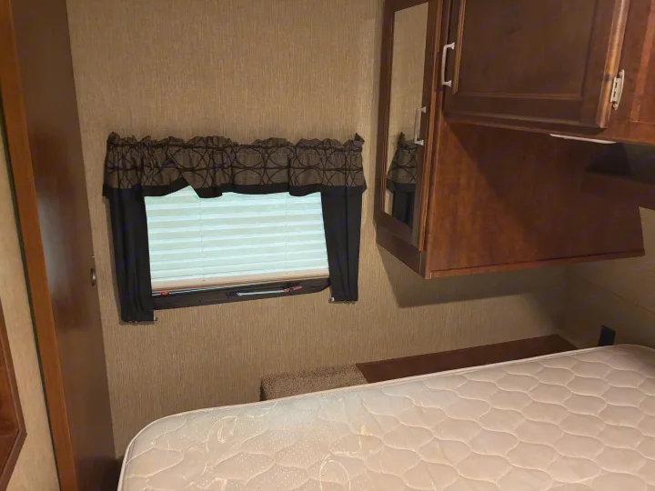 RV rental bedroom interior with a bed, window, and cabinet, offering a cozy space for travel.. Keystone RV Outback Ultra-Lite 2017