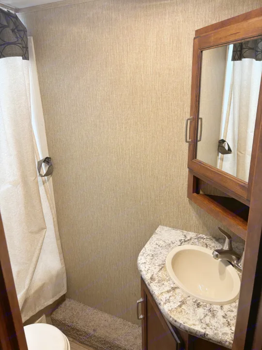 Compact RV rental bathroom features a sink, mirrored cabinet, shower, and neutral textured walls.. Keystone RV Outback Ultra-Lite 2017