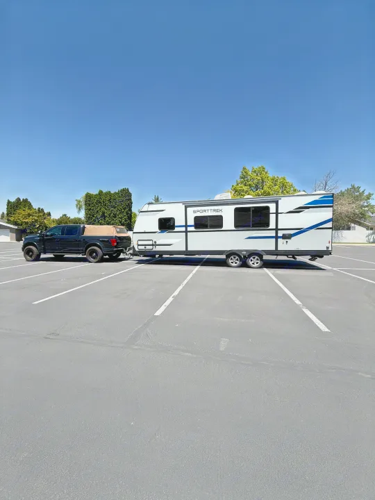 Discover adventure with this SportTrek RV rental, towed by a pickup truck in a large, sunny parking lot.. Sport Trek 270 VBH 2021