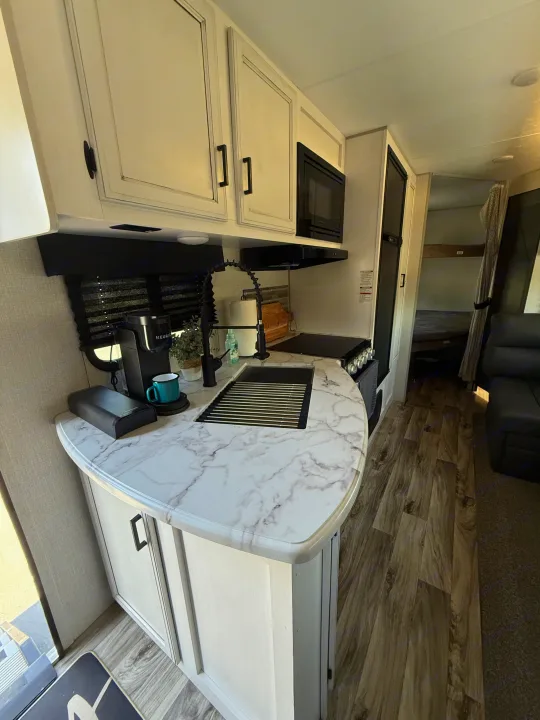 This RV rental features a modern kitchen with marbled counters, sink, black appliances, and Keurig. A living area and bunk beds are visible.. Sport Trek 270 VBH 2021