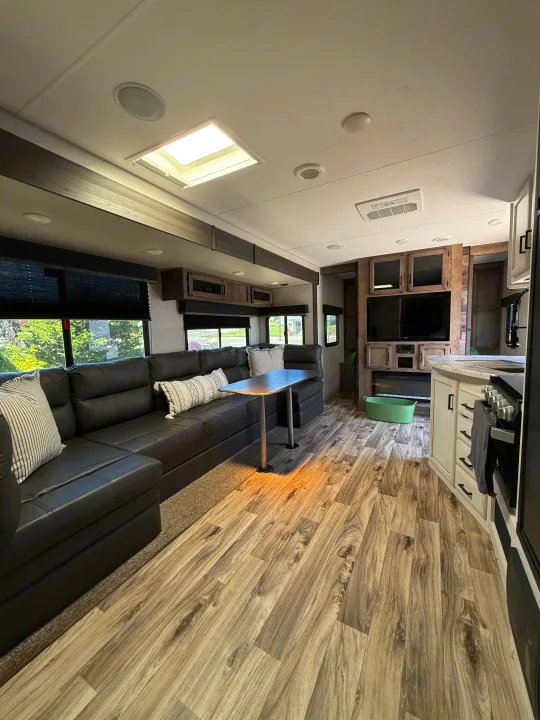 Modern RV rental interior with a spacious living area featuring a large black sectional, light wood-look flooring, and entertainment.. Sport Trek 270 VBH 2021