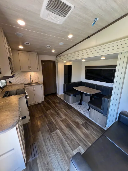 Modern RV rental interior: light kitchen cabinets, black dinette, and wood-look flooring, offering comfort on the go.. Keystone RV Cougar 2023
