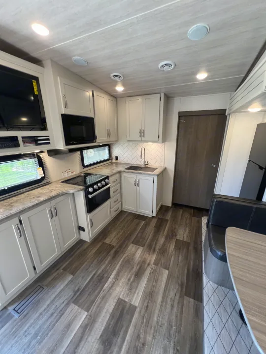 Inside a clean RV rental: modern kitchen with light cabinets, appliances, sink, and wood-patterned flooring.. Keystone RV Cougar 2023